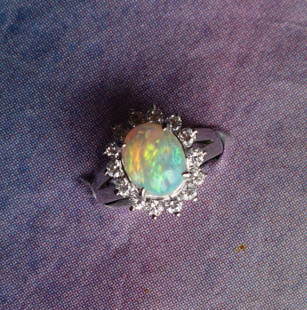 An opal and diamond ring set with a cabochon oval opal and a halo of round brilliant cut diamonds