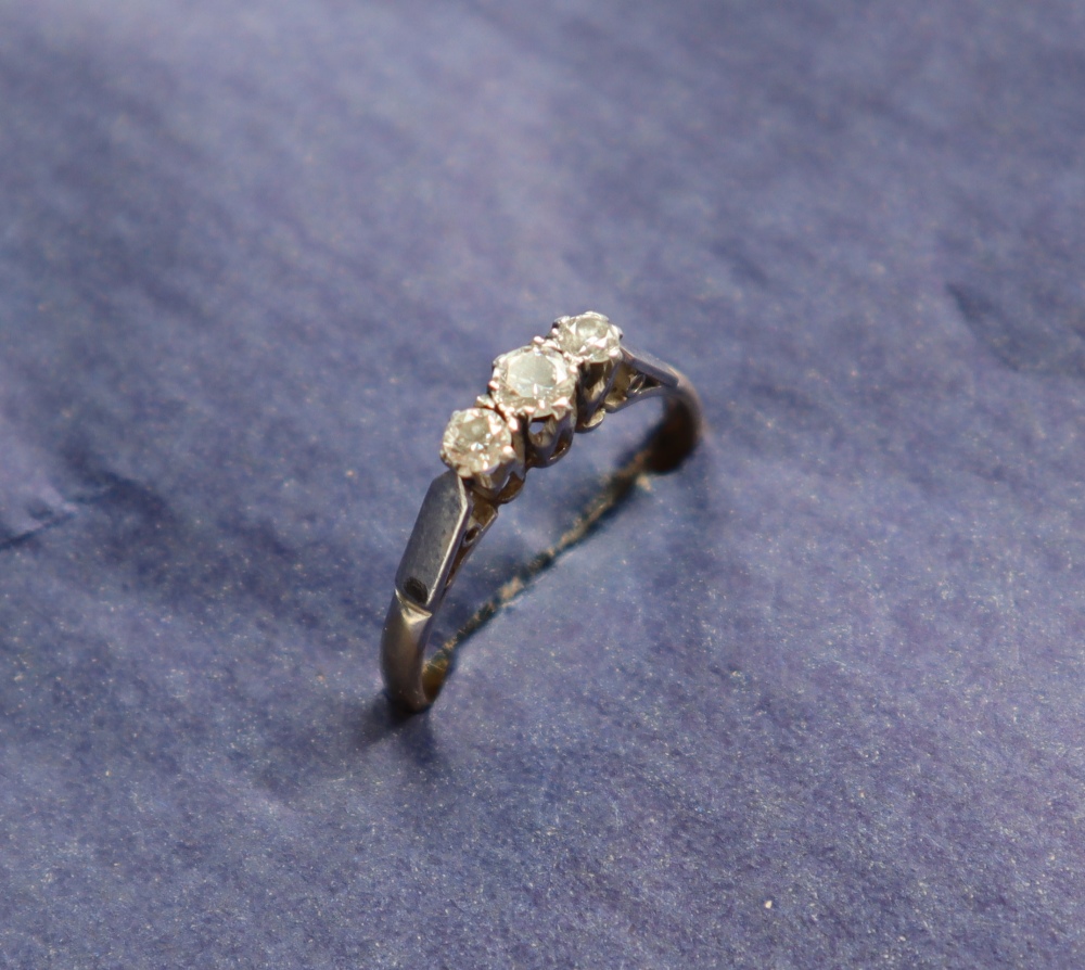 A three stone diamond ring set with round old cut diamonds of graduating sizes to a white metal