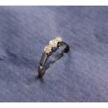 A three stone diamond ring set with round old cut diamonds of graduating sizes to a white metal