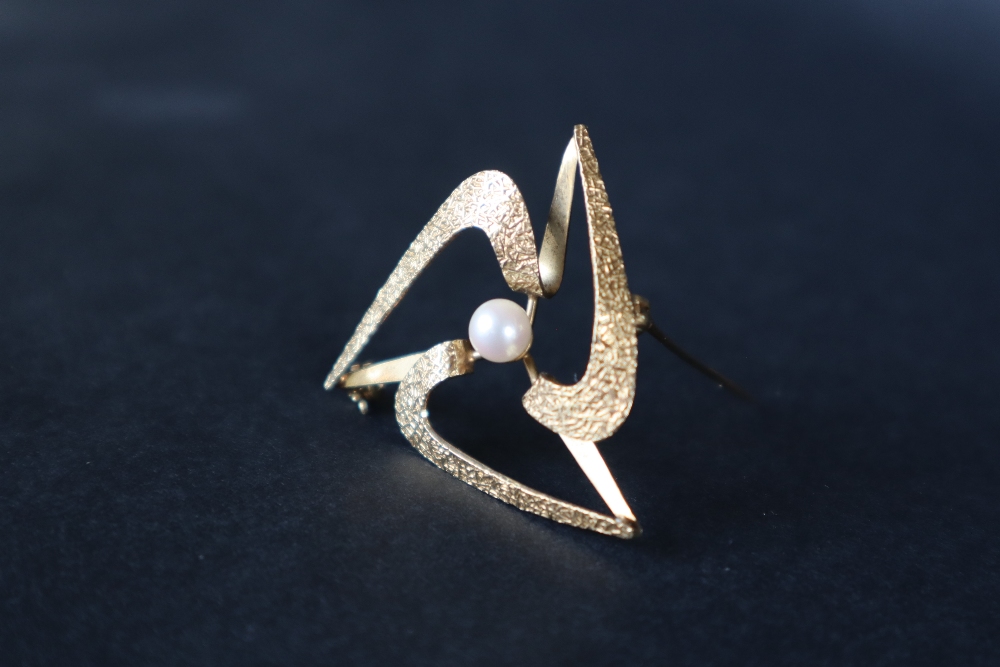 A 9ct textured yellow gold star shaped brooch, set with a central pearl, 3.
