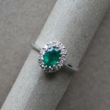 An emerald and diamond cluster ring set with an oval faceted emerald surrounded by round brilliant