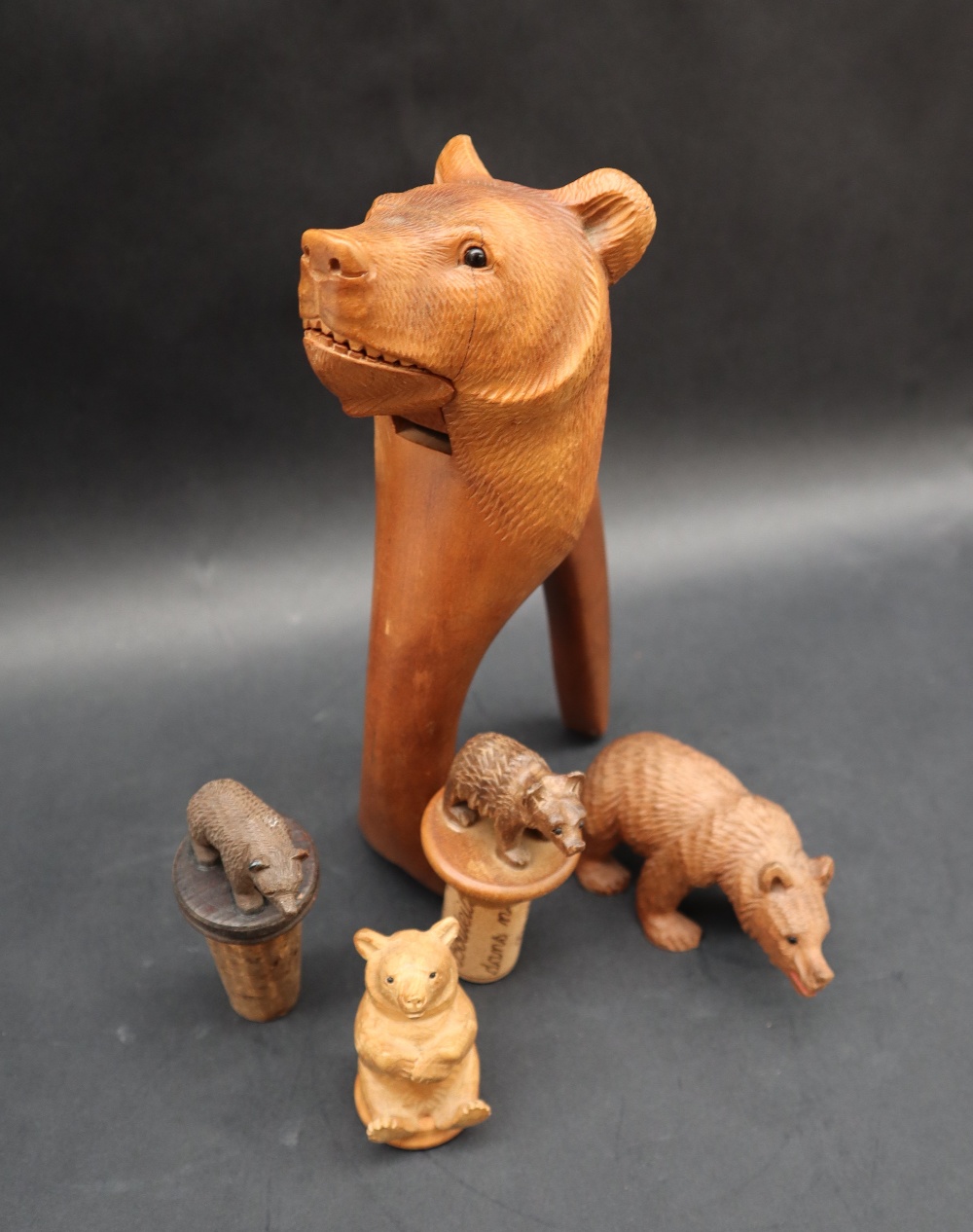 A Black Forest carved Bear lever nut cracker together with two carved bear topped bottle stops,
