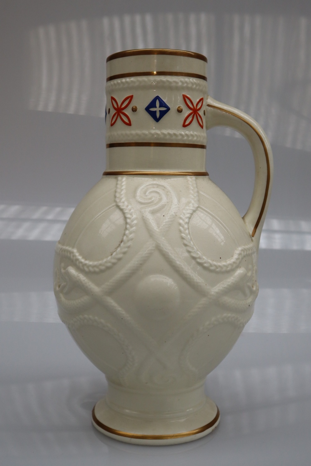 A Victorian pottery creamware jug with a cylindrical neck and bulbous body decorated with serpents