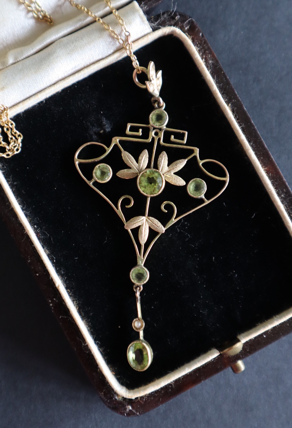 A yellow metal peridot and seed pearl pendant of heart and leaf shape on a yellow metal chain