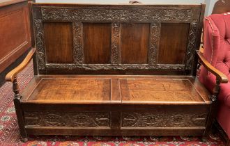 A 19th century carved oak settle with a four panelled back and box seats on turned feet