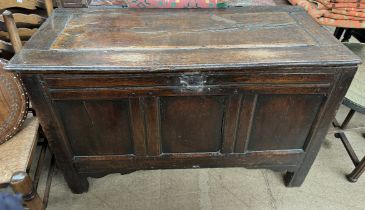 An 18th century oak coffer with a rectangular top above a three panel front on stiles