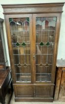 An Art Nouveau inspired bookcase with a moulded cornice above a pair of glazed doors with coloured