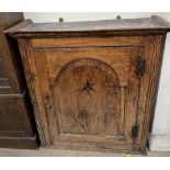 A 19th century oak cupboard with a moulded cornice above an inlaid arched panel door,
