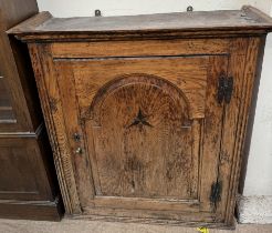 A 19th century oak cupboard with a moulded cornice above an inlaid arched panel door,