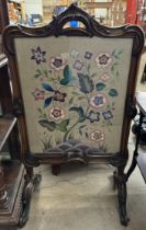 A 19th century walnut framed fire screen with a leaf moulded scrolling handle to the top,