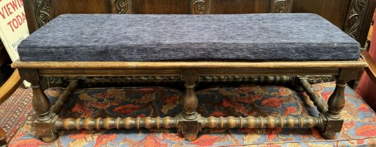 An oak stool with a pad upholstered top on baluster legs united by a barley twist stretcher