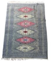A hand knotted woollen rug with a light grey green field, six red / cream diamond shaped medallions