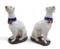 A pair of pottery sculptures, modelled as white greyhounds, wearing blue collars with red tassels,