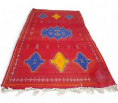 A Moroccan kilim rug, on red ground with traditional Berber symbols and blue and yellow