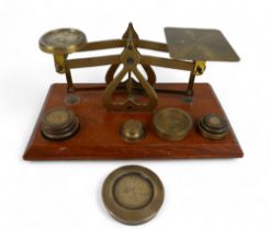 A set of brass postal scales on wooden base with ten brass weights, 18cm by 10cm by 8cm tall.