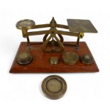 A set of brass postal scales on wooden base with ten brass weights, 18cm by 10cm by 8cm tall.