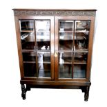 A 1930s oak bookcase, with blind carved frieze above two glazed doors