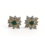 A pair of diamond and emerald flowerhead earrings, each comprising eight brilliant cut diamonds