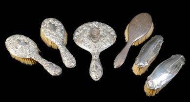 A group of silver-backed dressing table items, comprising a hand mirror, two brushes with repousse
