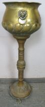 An antique brass pedestal jardinière planter, having relief decoration depicting an armorial crest