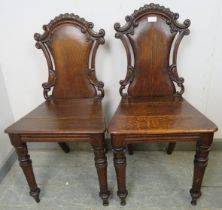 A pair of 19th century oak hall chairs, having scroll carved and pierced backs, on carved tapered