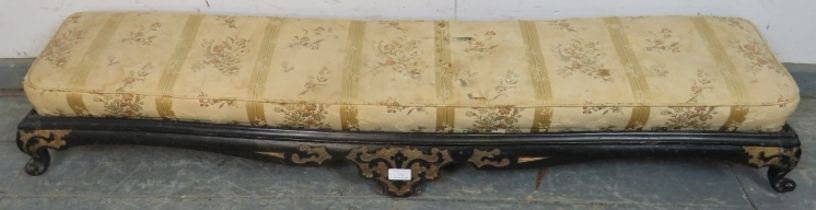 A 19th century long low footstool, with loose cushion, the ebonised base with relief decoration