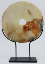 A Chinese white and russet jade bi disc, Neolithic style, probably late 19th/20th century. Supported