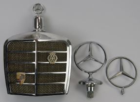 Automobilia: A vintage Mercedes Benz car grill drinks decanter flask and two car bonnet emblems,