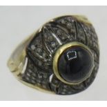 A yellow & white metal ring set with a dark cabochon sapphire and several panels of rose cut