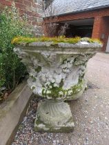 A nicely weathered reconstituted stone garden urn on stand, having relief moulded decoration in