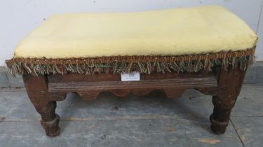 A 17th century, possibly earlier, oak footstool, upholstered in yellow damask, with shaped apron