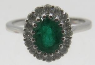 An 18ct white gold oval emerald & diamond cluster ring, size M. Emerald approx 1.31cts, round