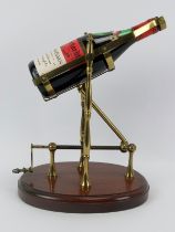 A brass mechanical wine decanting cradle. Supported on an oval oak plinth. Bottle of Jacob