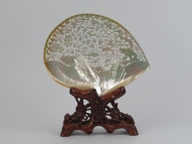 A large Chinese carved and pierced mother of pearl shell mounted on a carved wood stand, mid/late