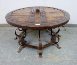 A low circular coffee table fashioned from a medieval cartwheel with iron strapwork mounts, on a