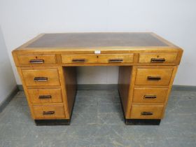 An Art Deco Period light oak pedestal desk, housing a configuration of nine graduated drawers with