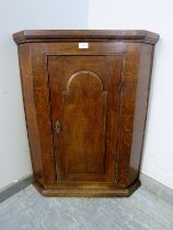 A Georgian oak hanging corner cupboard, the door with arched panel decoration, opening onto two