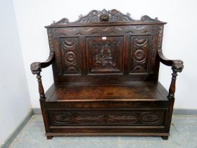 A 19th century Gothic Revival oak settle, the backrest with relief carved decoration depicting