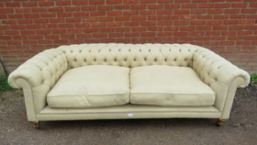 An antique three-seater Chesterfield sofa, reupholstered in neutral buttoned material, on fluted