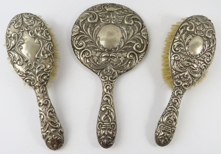 A three piece silver backed vanity set including two brushes and a mirror. All hallmarked for