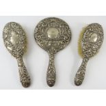 A three piece silver backed vanity set including two brushes and a mirror. All hallmarked for