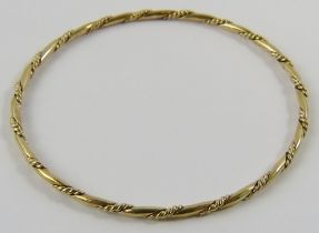 A solid yellow precious metal hoop bangle with rope twist, testing as 9ct yellow gold. Total