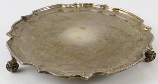 A small silver salver card tray with piecrust edge and standing on three foliate feet. Hallmarked