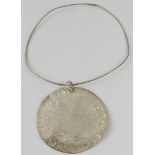 A large silver Artisanal disc pendant, 7.8cm diameter approx, on silver wire collar, with feature