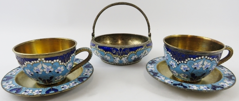 Two Russian silver gilt and enamel cups and saucers and a matching sugar basket. Each with enamelled