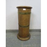An early 20th century coopered light oak cylinder stick stand, having a tin liner, on a plinth base.