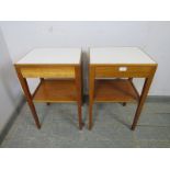 A pair of mid-century teak two-tier side tables, the inset formica tops above blind drawers, on