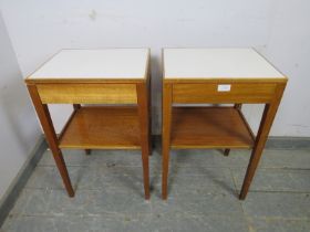 A pair of mid-century teak two-tier side tables, the inset formica tops above blind drawers, on