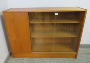 A mid-century teak low enclosed bookcase, having sliding glass doors opening onto two loose shelves,
