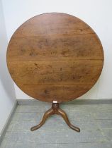 A Georgian oak tilt-top circular supper table, on a tapered turned column with splayed tripod